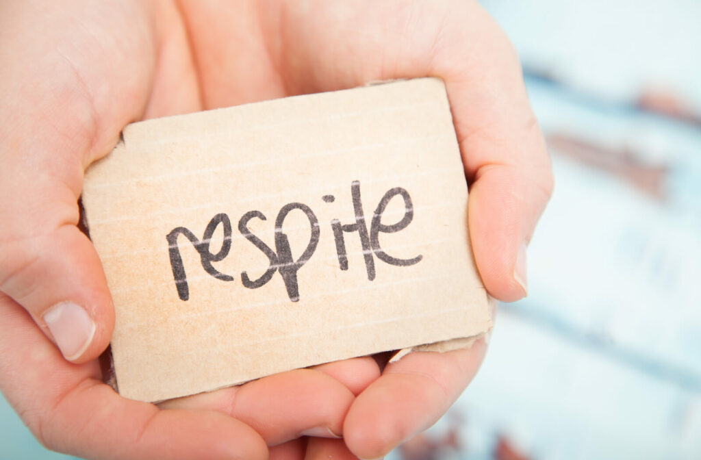 a pair of hands hold a piece of paper with respite written on it in black pen