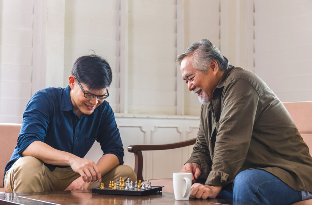 A happy senior person playing chess with his young son in the living room.